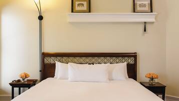 A neatly made bed with white linens, a wooden headboard with a diamond pattern, and a white nightstand with a vase of flowers.