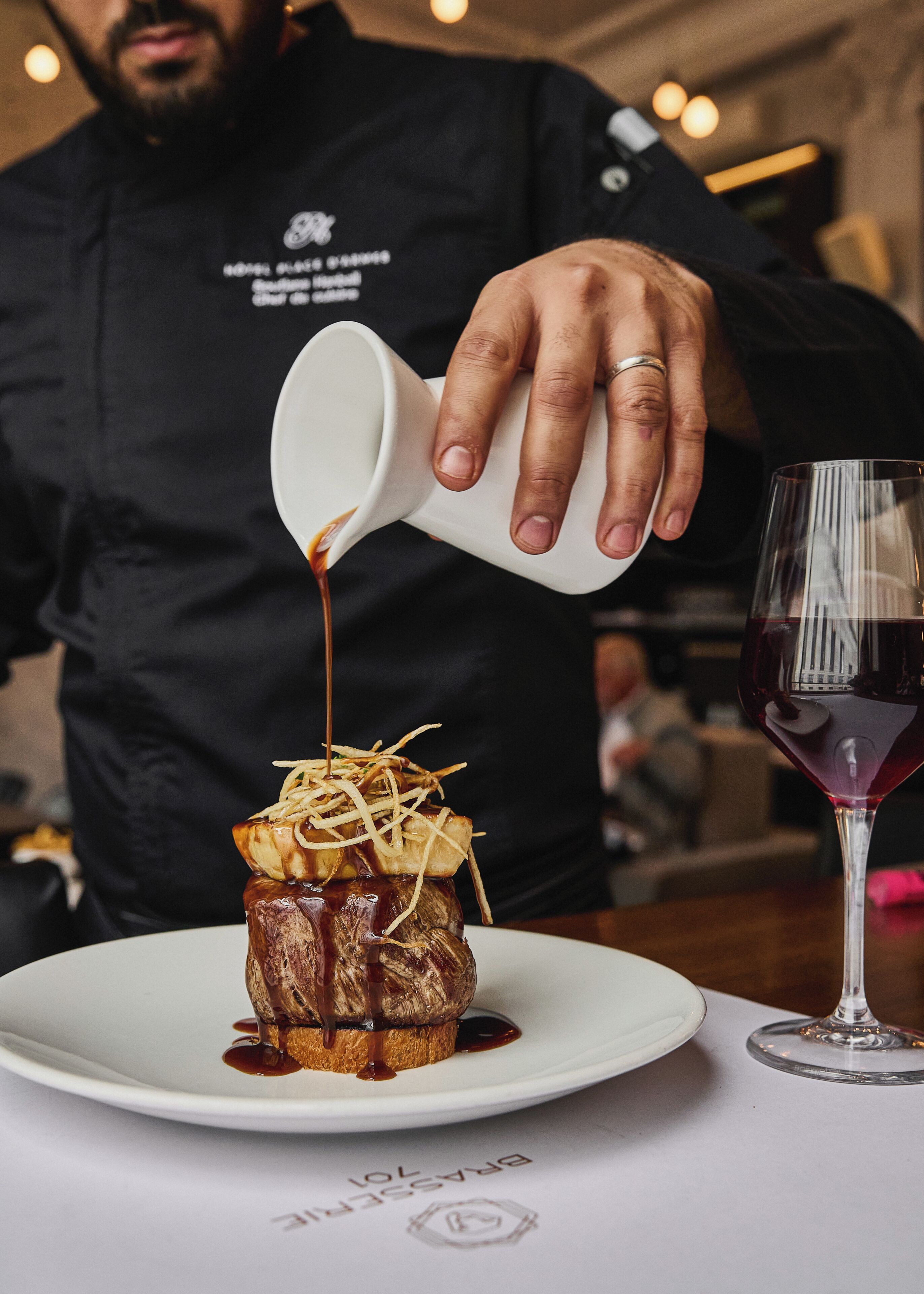 A person pouring a sauce over a dessert on a plate.