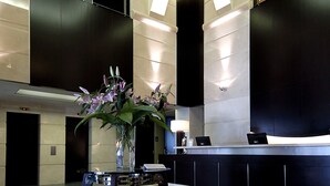 A modern lobby with a reception desk, a vase with flowers, and a geometric floor pattern. - Hotel Place d'Armes (Montreal)