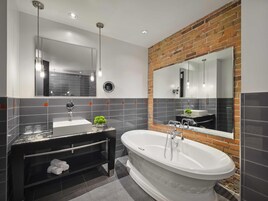 A modern bathroom with a black vanity, a freestanding bathtub, and a large mirror with a brick accent wall.