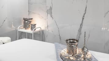 A hotel room with a marble wall, a bed with a white and blue striped blanket, and a small table with silver items.