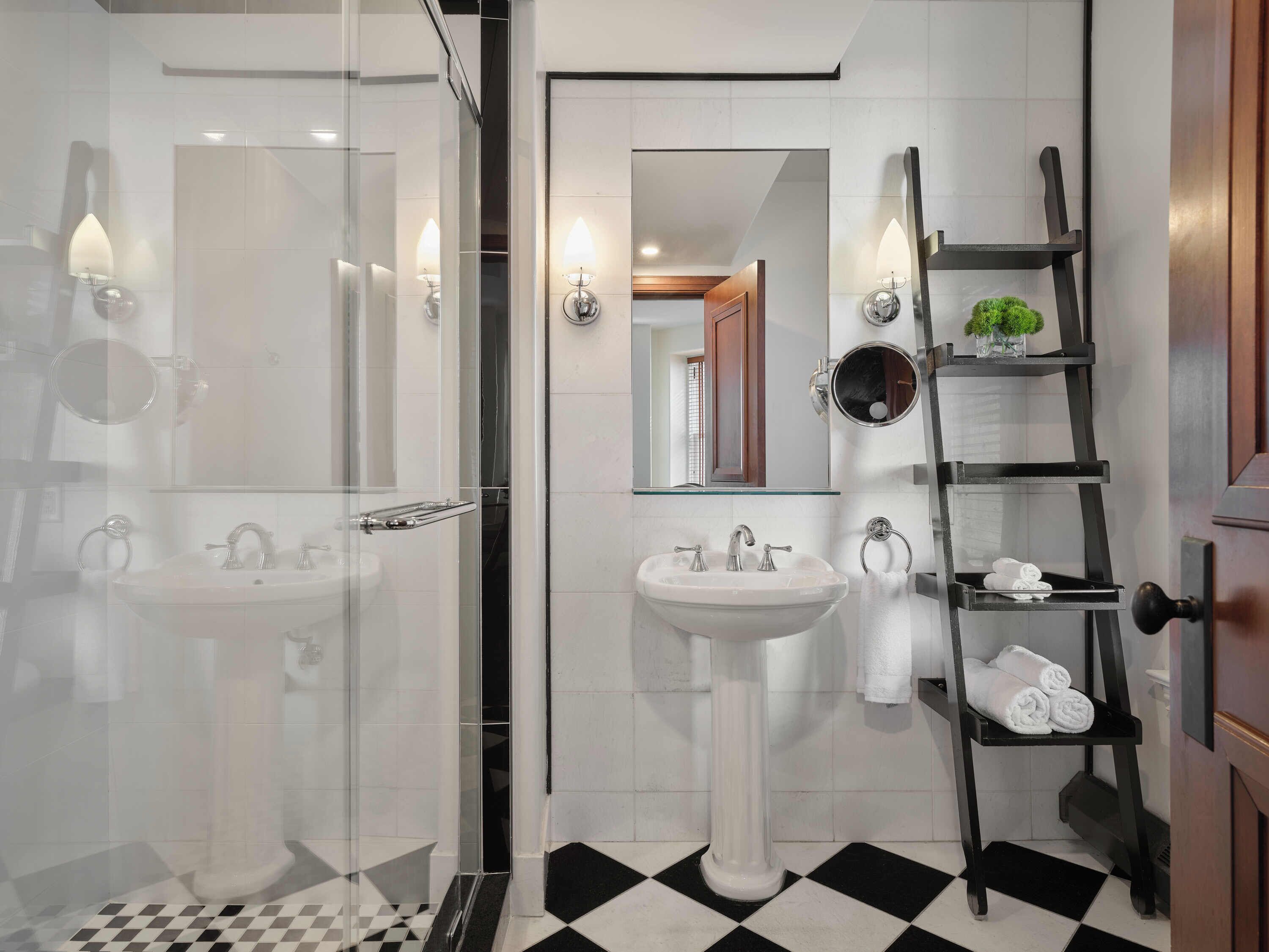 A modern bathroom with a glass shower enclosure, a pedestal sink, and a black and white checkered floor.