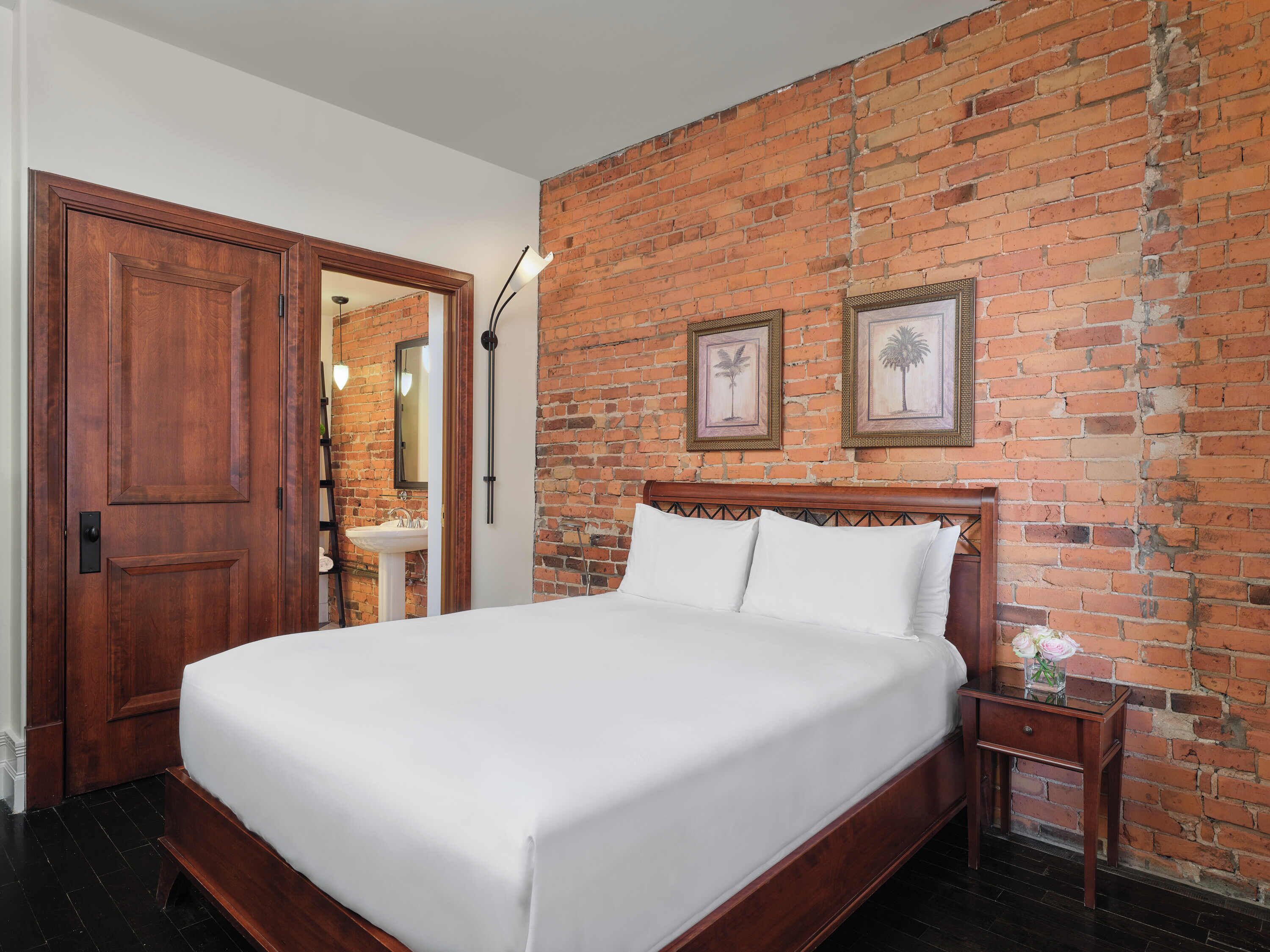 A bedroom with a wooden bed, a nightstand, a brick wall, and a door.