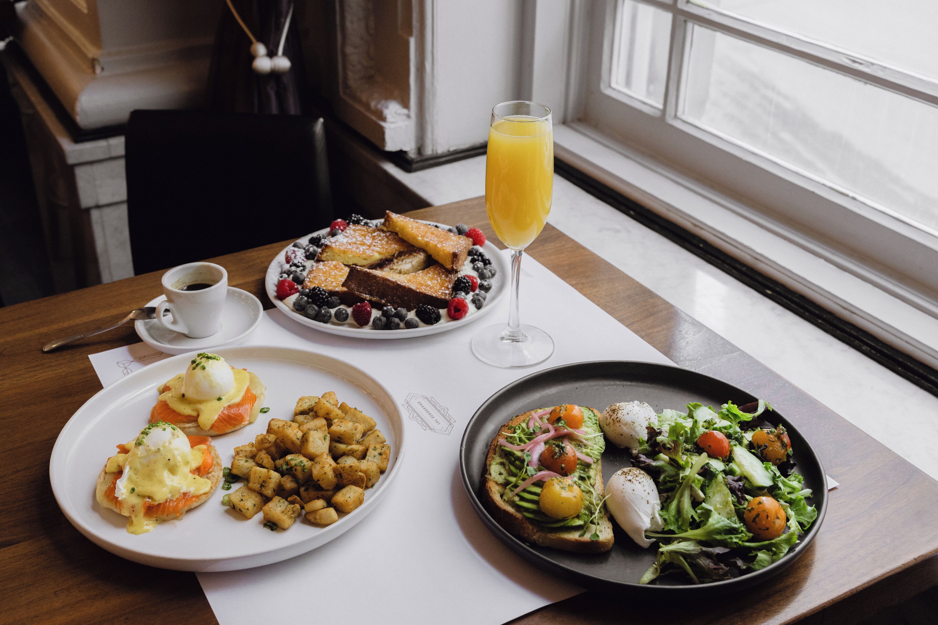 A breakfast table with various dishes including eggs benedict, toast, potatoes, and a salad.