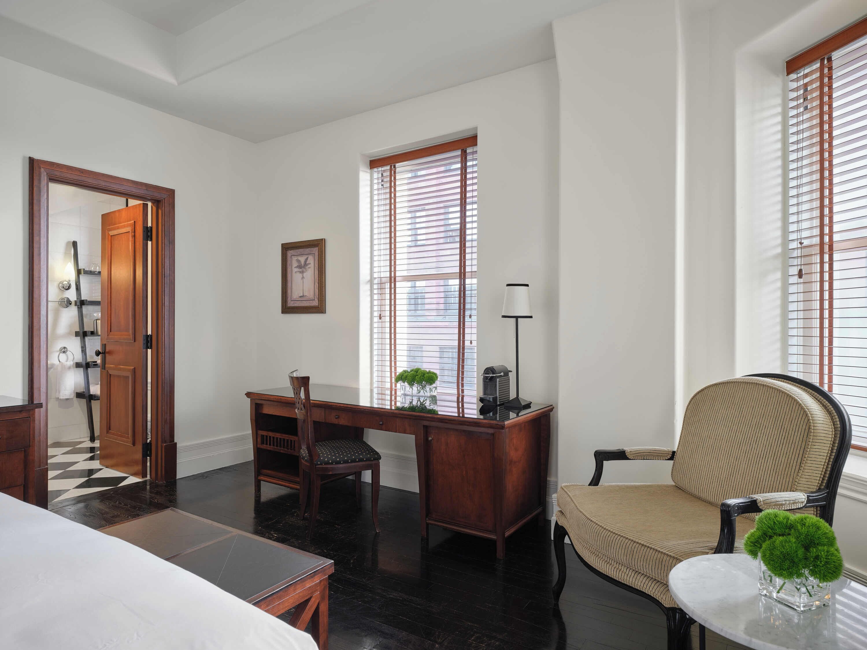 A room with a wooden desk, a chair, a small table with a vase, and a bed.