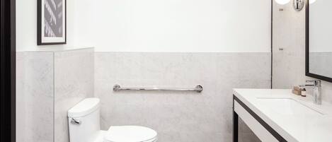 Un baño moderno con inodoro blanco, suelo a cuadros blanco y negro, lavamanos blanco con espejo arriba y un cuadro enmarcado en la pared.