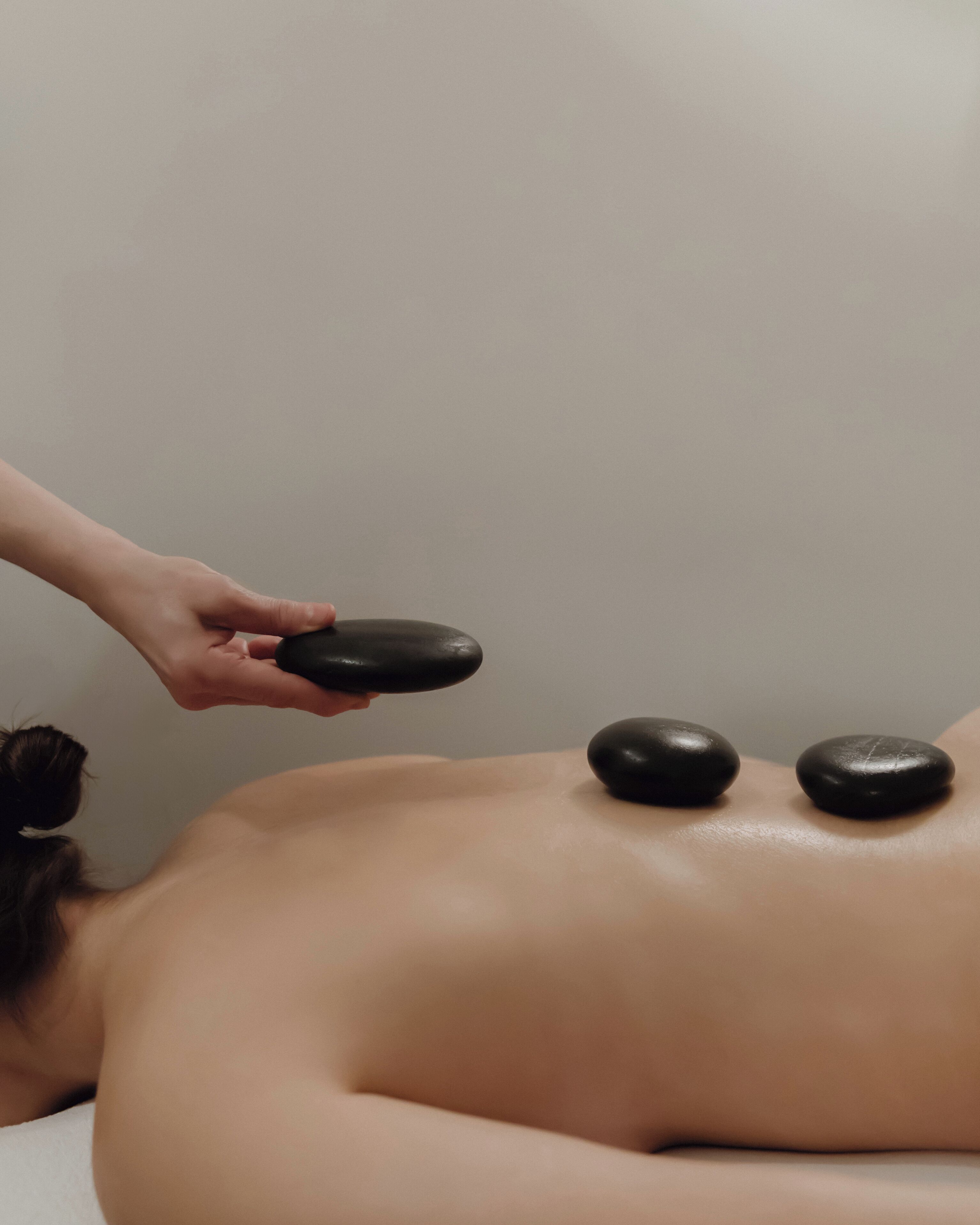 A person receiving a back massage with two black stones placed on their back.