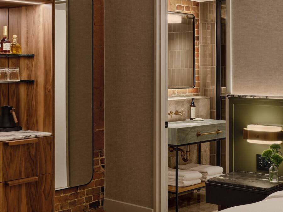 A hotel room with a wooden wardrobe, a marble-topped vanity, a bedside table with a lamp, and a bed with a green headboard.
