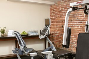 A gym with exercise equipment, a digital screen, and a brick wall.