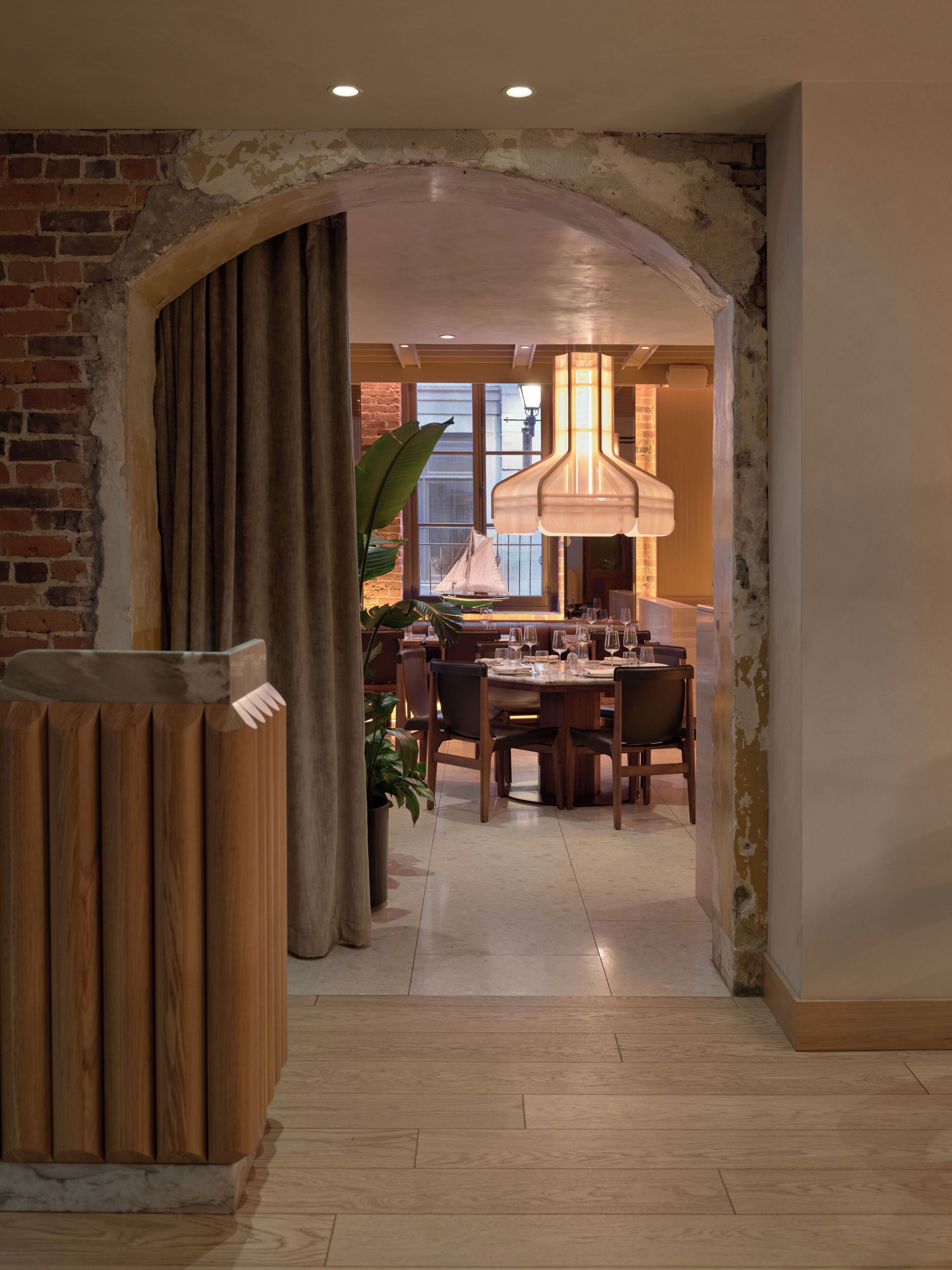 Un interior con zona de comedor, suelo de madera, pared de ladrillo y una planta grande.
