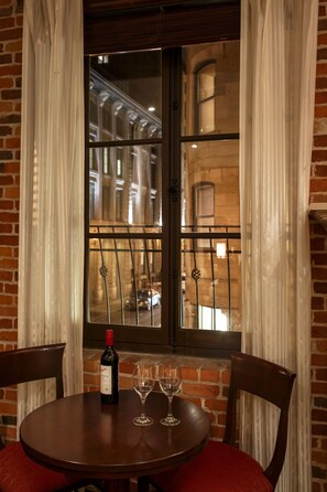 A round table with a bottle of wine and two glasses, set against a brick wall with a window overlooking a street. - Hotel Nelligan (Montreal)