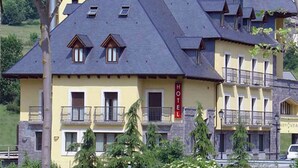 Un hotel con varios balcones, un llamativo letrero que dice 'HOTEL' y un paisaje montañoso de fondo.