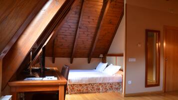 Un dormitorio con techo inclinado, vigas de madera, una cama con ropa blanca, un escritorio con silla y un espejo en la pared.