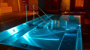 Un área de spa moderna y bien iluminada, con un jacuzzi de paredes de vidrio y escalones metálicos.