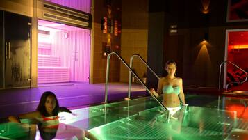 A glass-enclosed indoor swimming pool with metal railings and a purple-lit wall in the background.