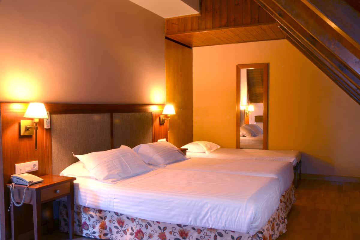 A hotel room with a bed, two bedside lamps, a nightstand with a phone, and a mirror on the wall.
