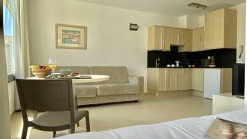 A compact hotel room with a dining area, kitchenette, and a bed with a magazine.