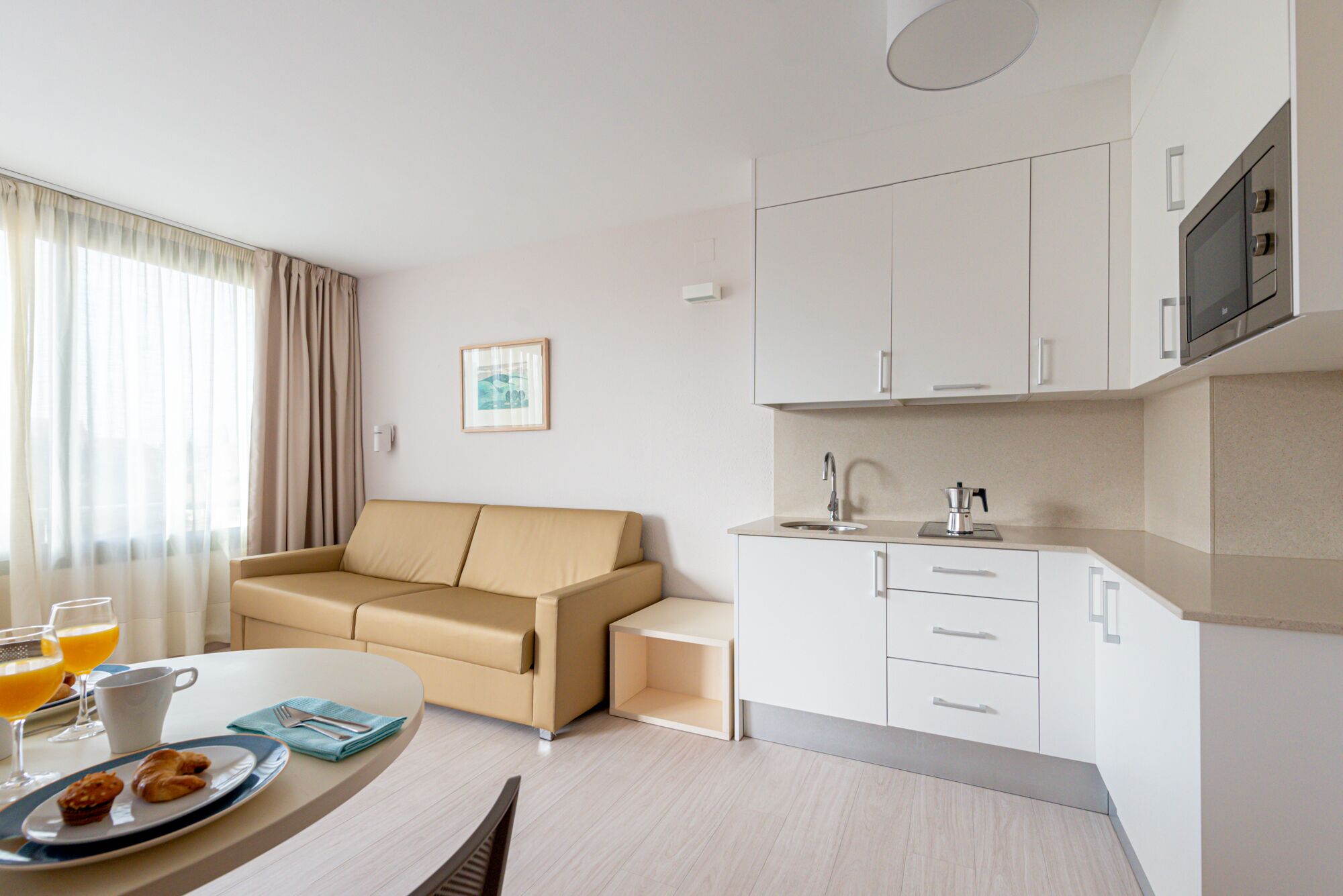 Una habitación de hotel moderna con sofá, una mesa de comedor con desayuno y una kitchenette.