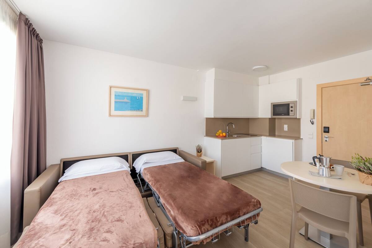Una habitación con dos camas, una kitchenette pequeña, un comedor y una puerta.