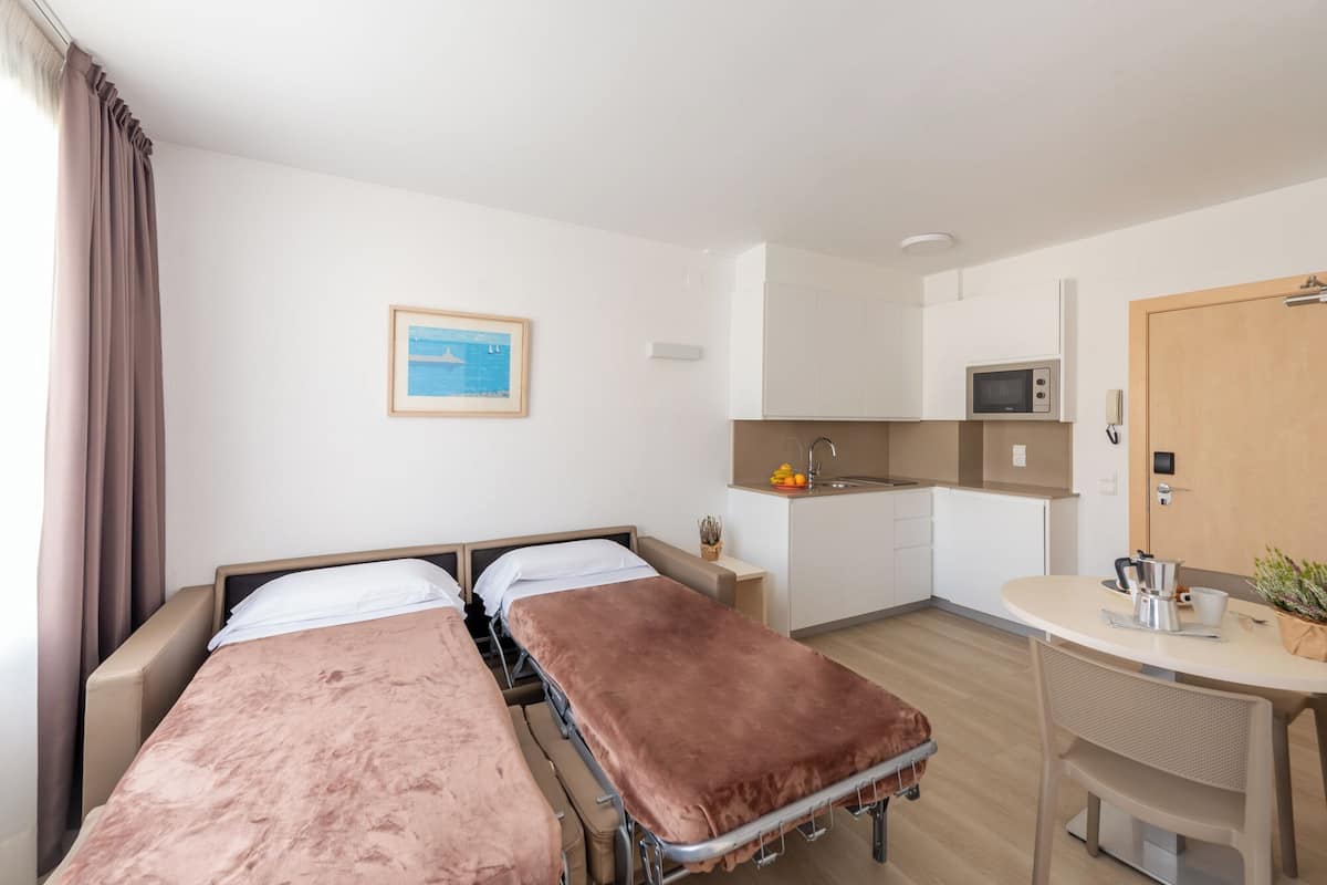 A room with two beds, a kitchenette, a small table, and a door.