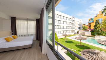 Een hotelkamer met een bed, uitzicht op een zwembad en een gebouw met balkons.