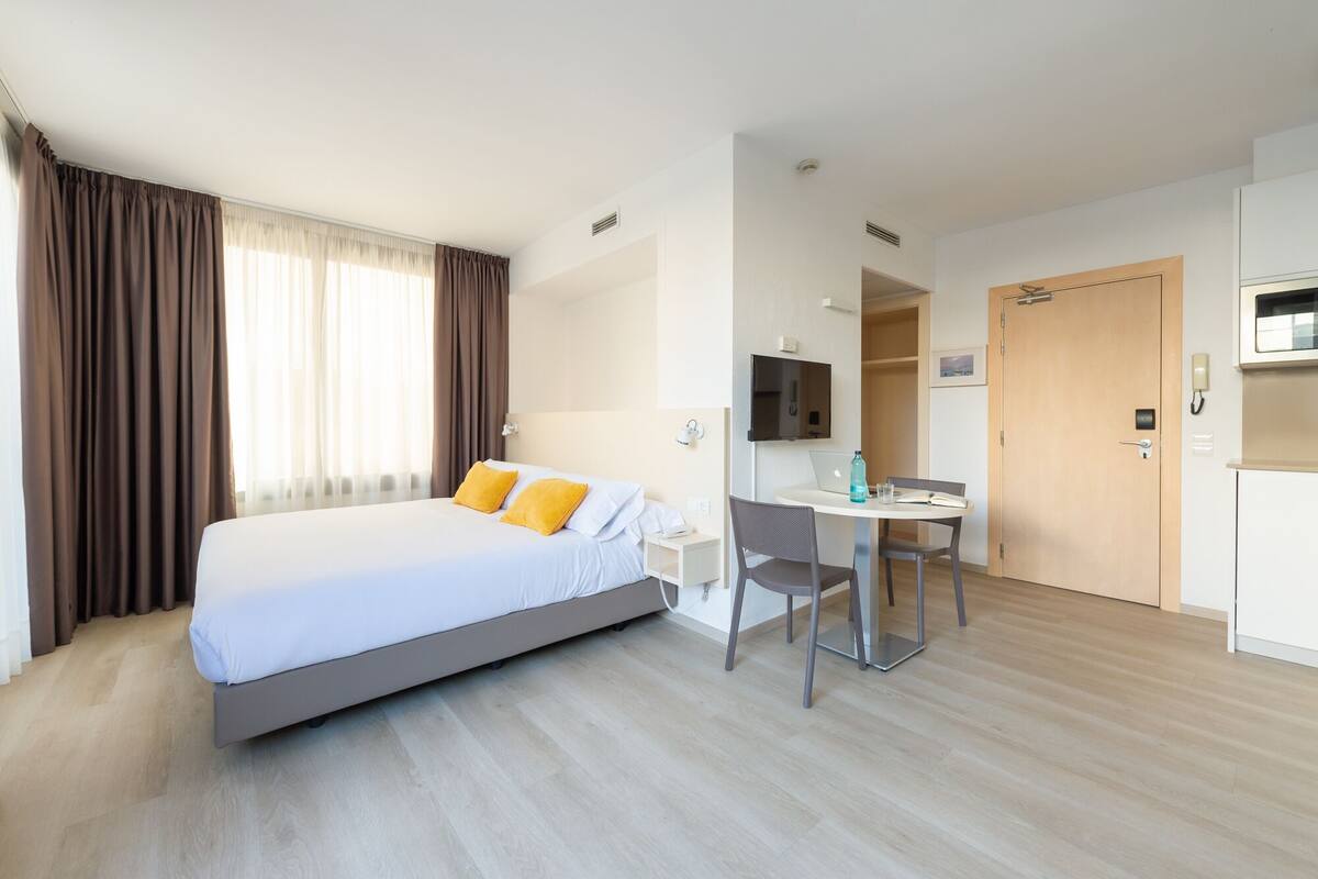 Una habitación de hotel con cama, escritorio, silla, televisor y puerta.