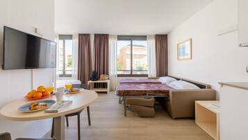 Una habitación de hotel con cama, escritorio, televisor y ventana con cortinas.