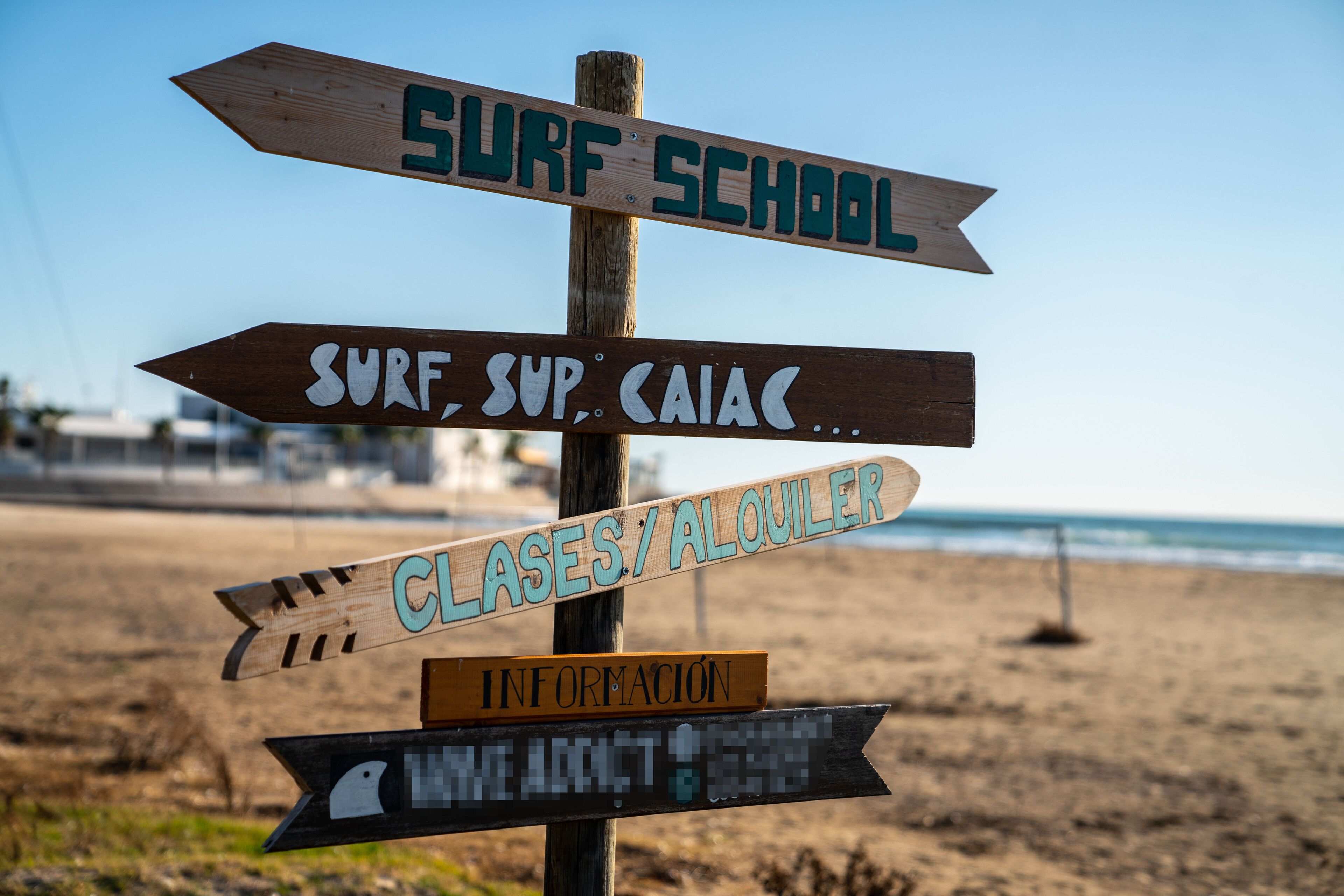 A wooden signpost with multiple directional signs, including one labeled "SURF SCHOOL".
