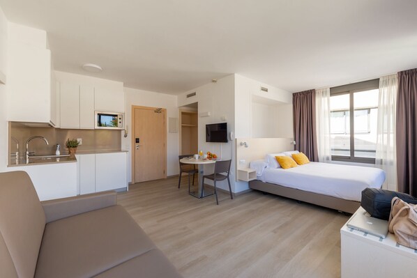 Una habitación de hotel compacta con kitchenette, una cama, una zona de estar y un televisor.