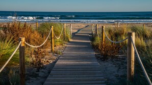 Un paseo marítimo de madera que conduce a la playa, rodeado de hierba y cuerdas.
