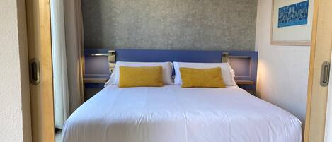 A double bed with white bedding and two yellow pillows, a nightstand with a lamp, and a framed picture on the wall.