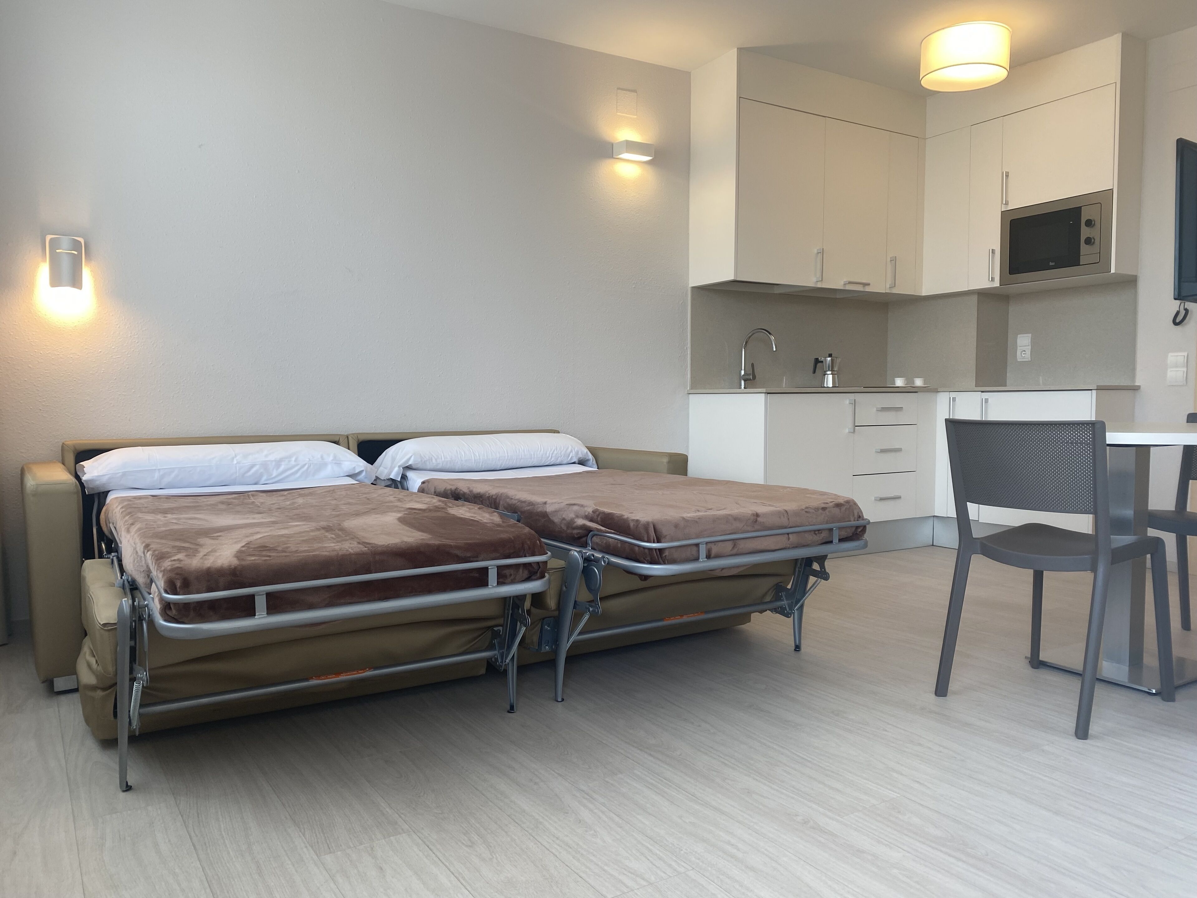 Habitación de hotel con dos camas, kitchenette y zona de comedor.