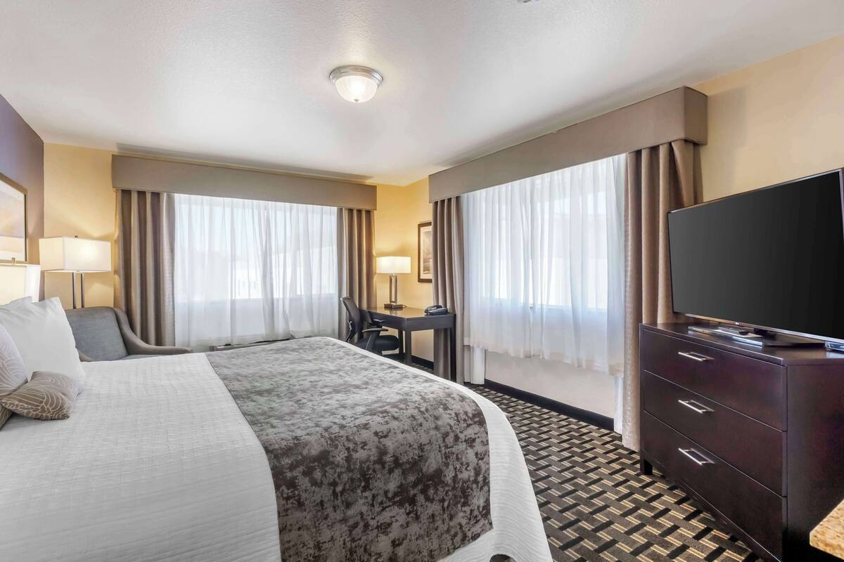 A hotel room with a large bed, a desk, a television, and a dresser.