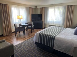 Habitación de hotel con cama, escritorio con silla, televisión y ventana con cortinas.