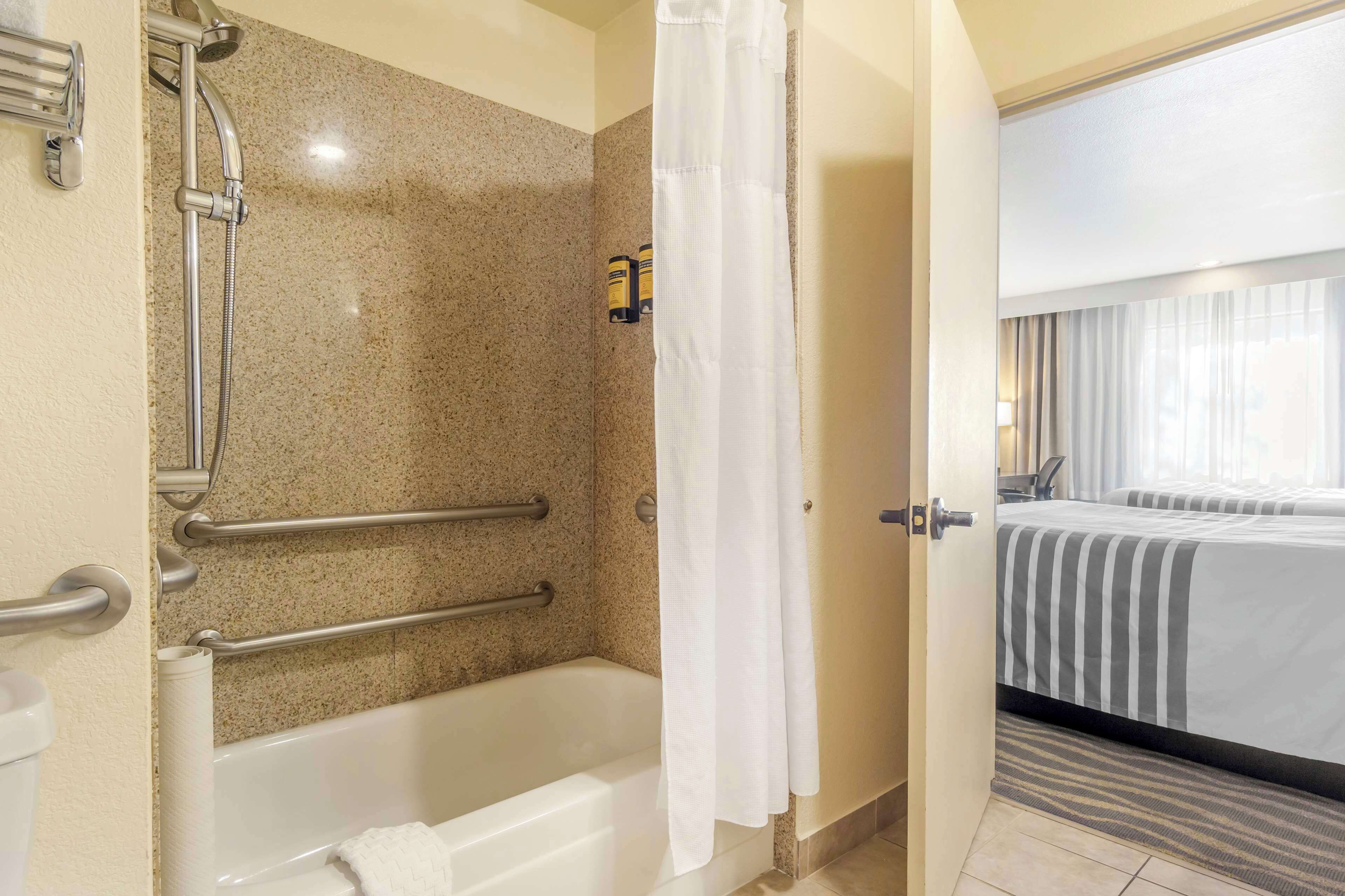 A bathroom with a bathtub, shower, and handrails.