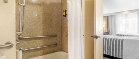 A bathroom with a bathtub, shower, and handrails.