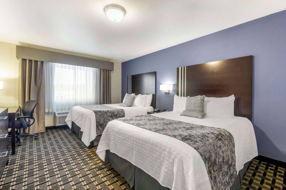 A hotel room with two beds, a desk, and a chair.
