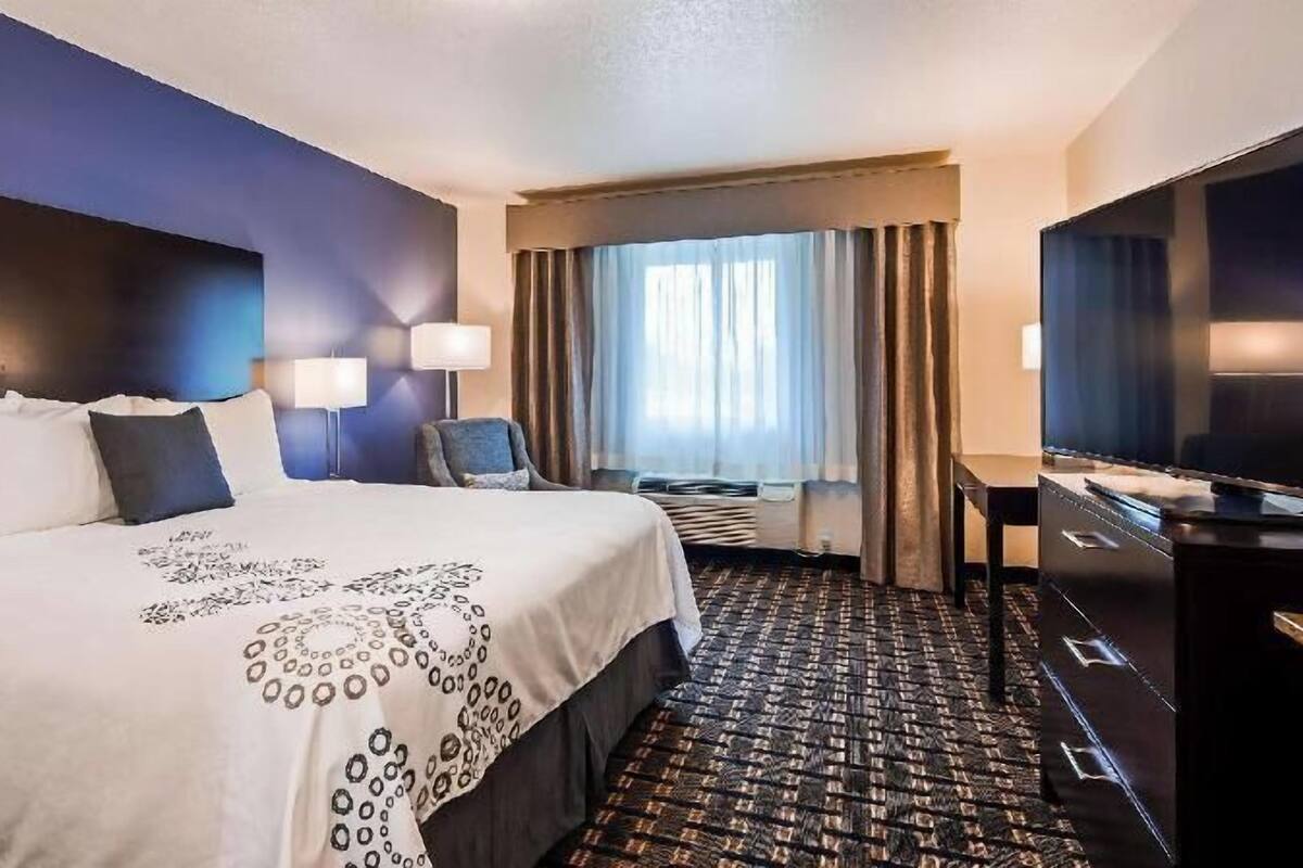 A hotel room with a large bed, a desk, a chair, a television, and a window with curtains.