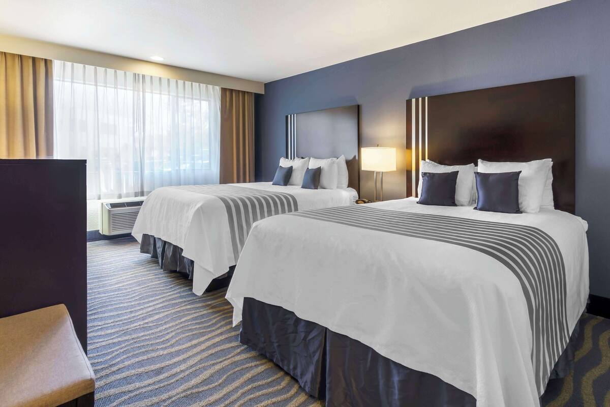 A hotel room with two beds, a TV, and a large window with curtains.