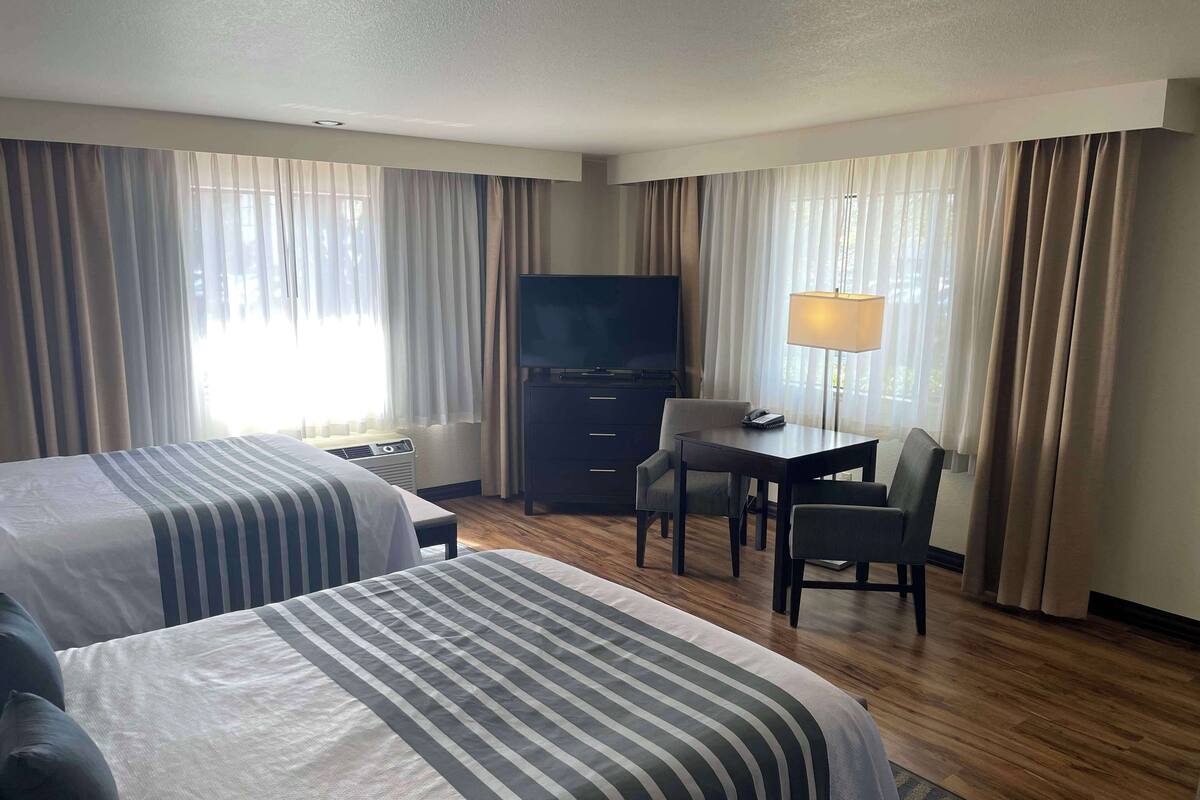 A hotel room with two beds, a desk with a chair, a television, and a lamp.