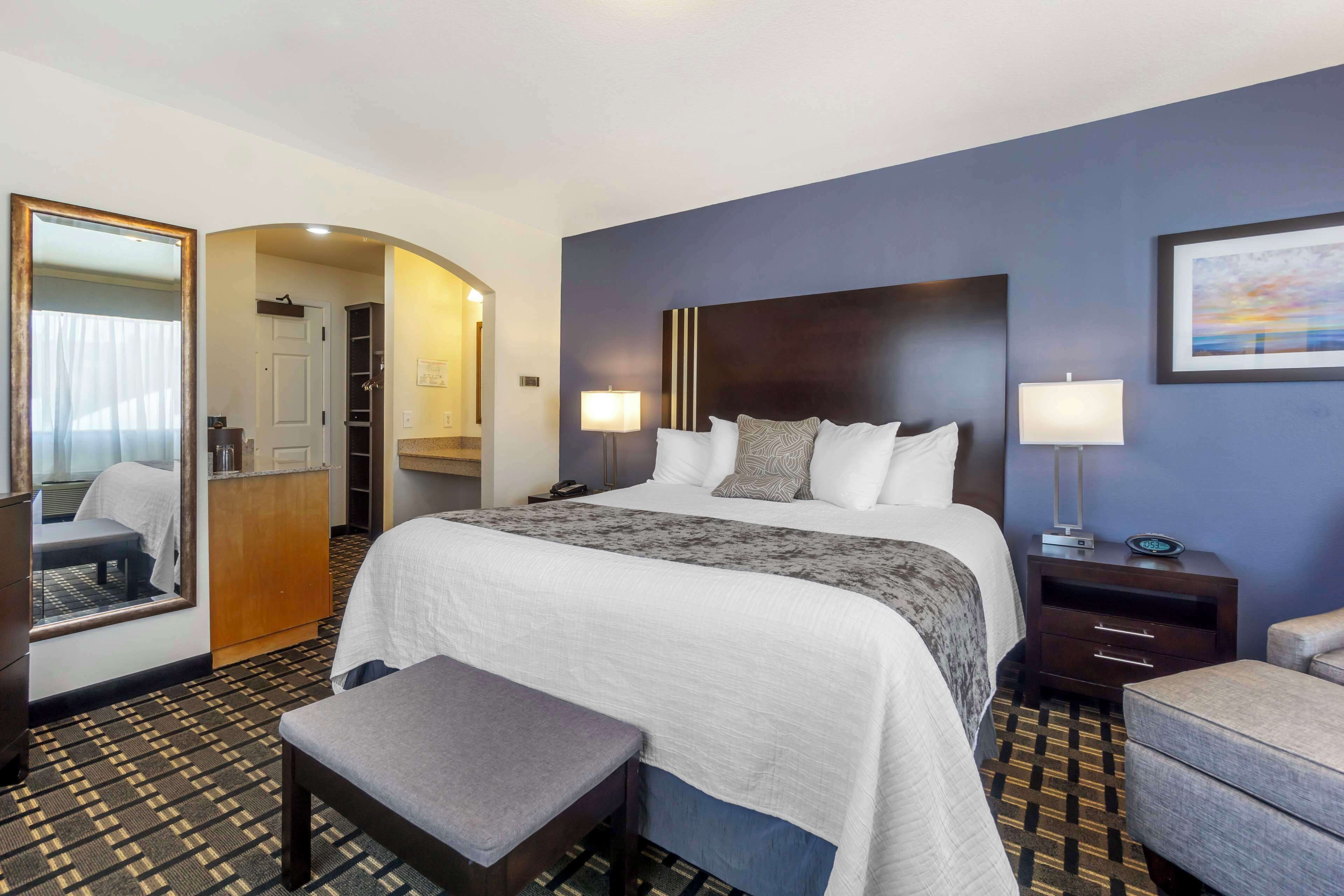 A hotel room with a large bed, bedside tables, a bench, a wardrobe, and a mirror.