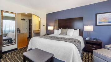 A hotel room with a large bed, bedside tables, a bench, a wardrobe, and a mirror.