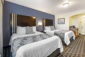 A hotel room with two beds, a desk, and a bathroom.
