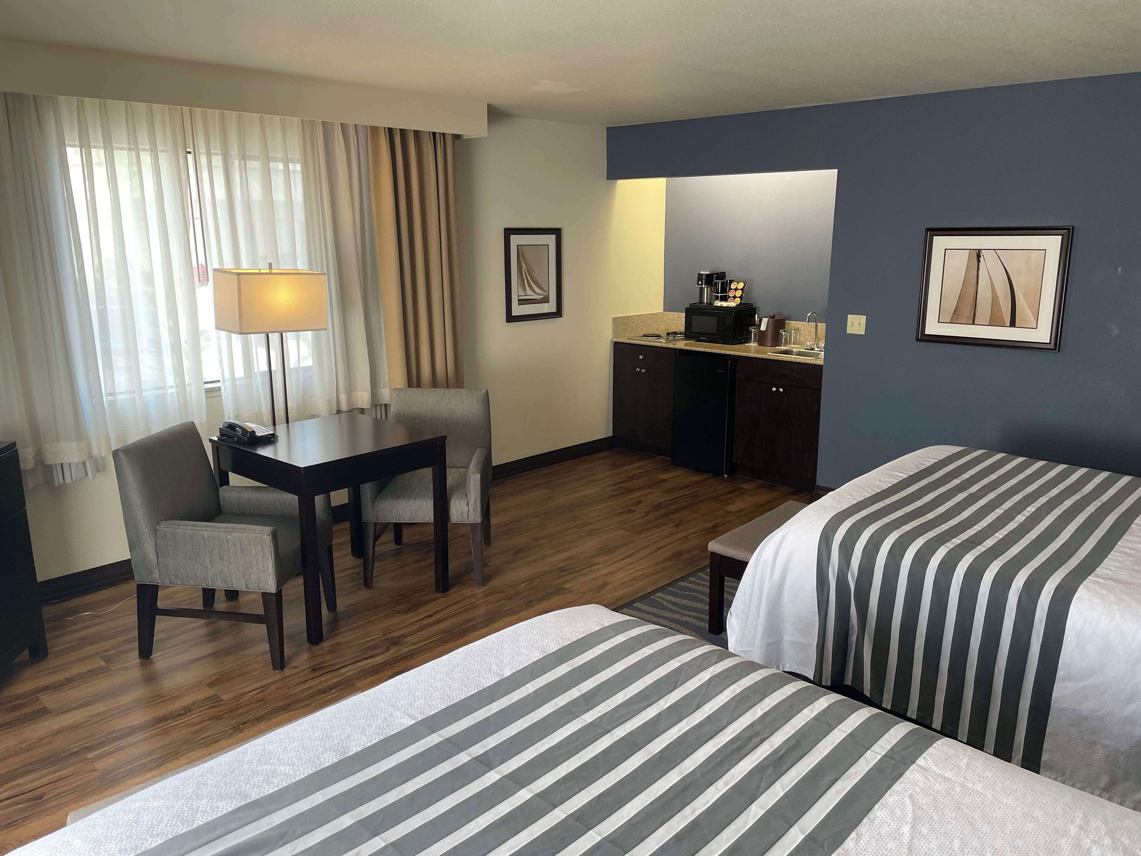 Een hotelkamer met een bureau, twee bedden, een kitchenette en een groot raam met gordijnen.