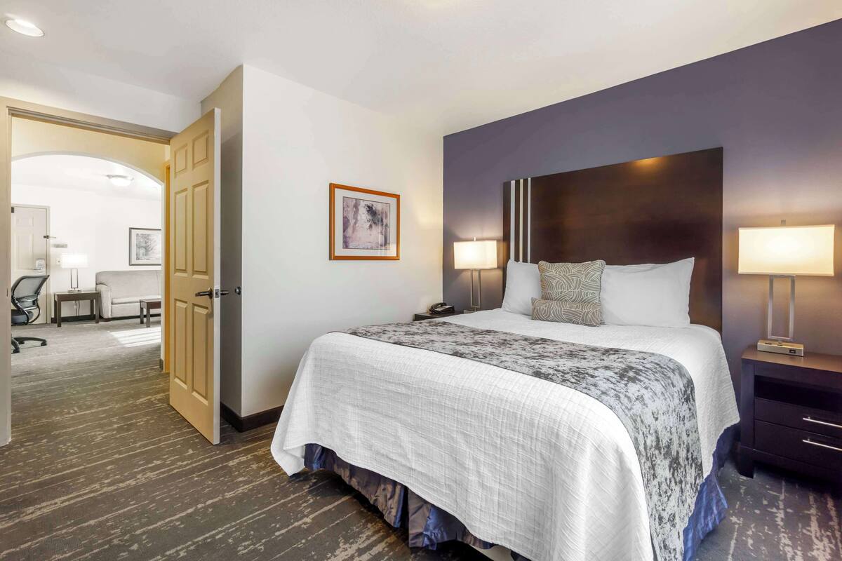 A hotel room with a large bed, two bedside lamps, a dark headboard, and a framed picture on the wall.