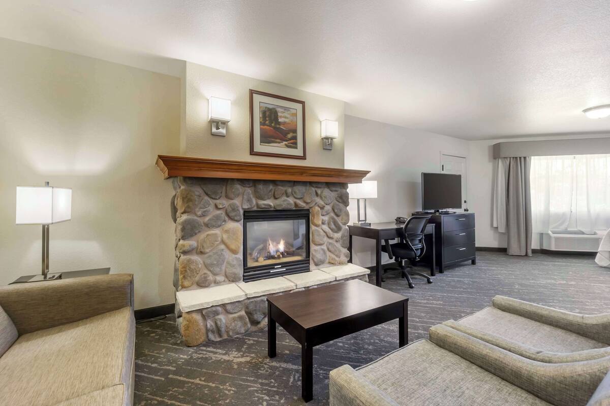 A hotel room with a stone fireplace, a desk, a television, and two armchairs.