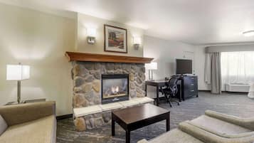 A hotel room with a stone fireplace, a desk, a television, and two armchairs.