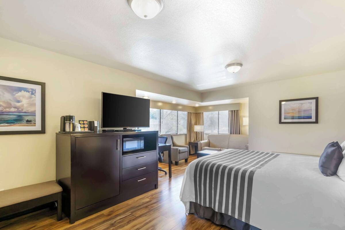 A hotel room with a bed, a desk with a flat-screen TV, a coffee maker, and a bench.