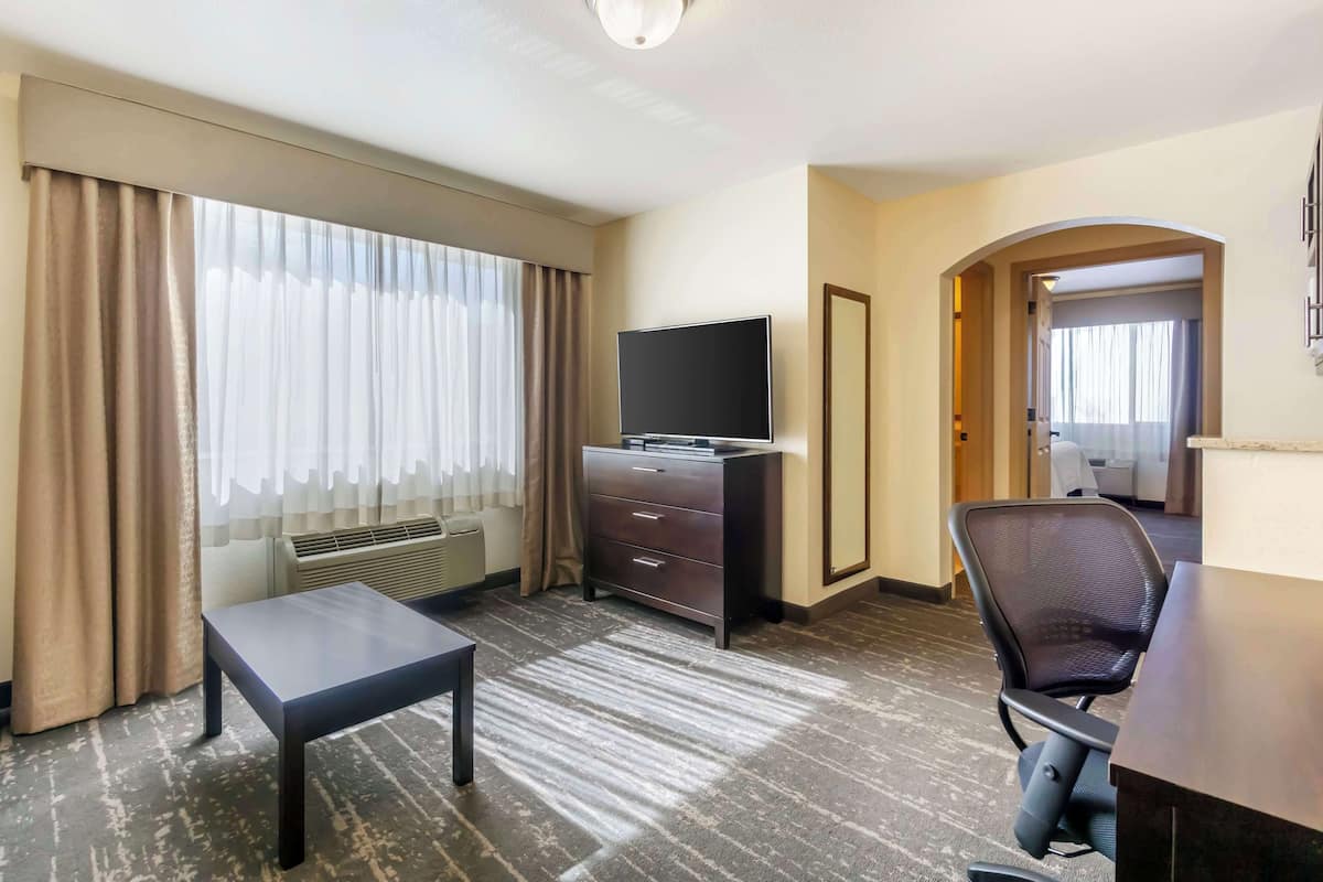 A hotel room with a flat-screen TV, a desk, a chair, a dresser, and a large window with curtains.