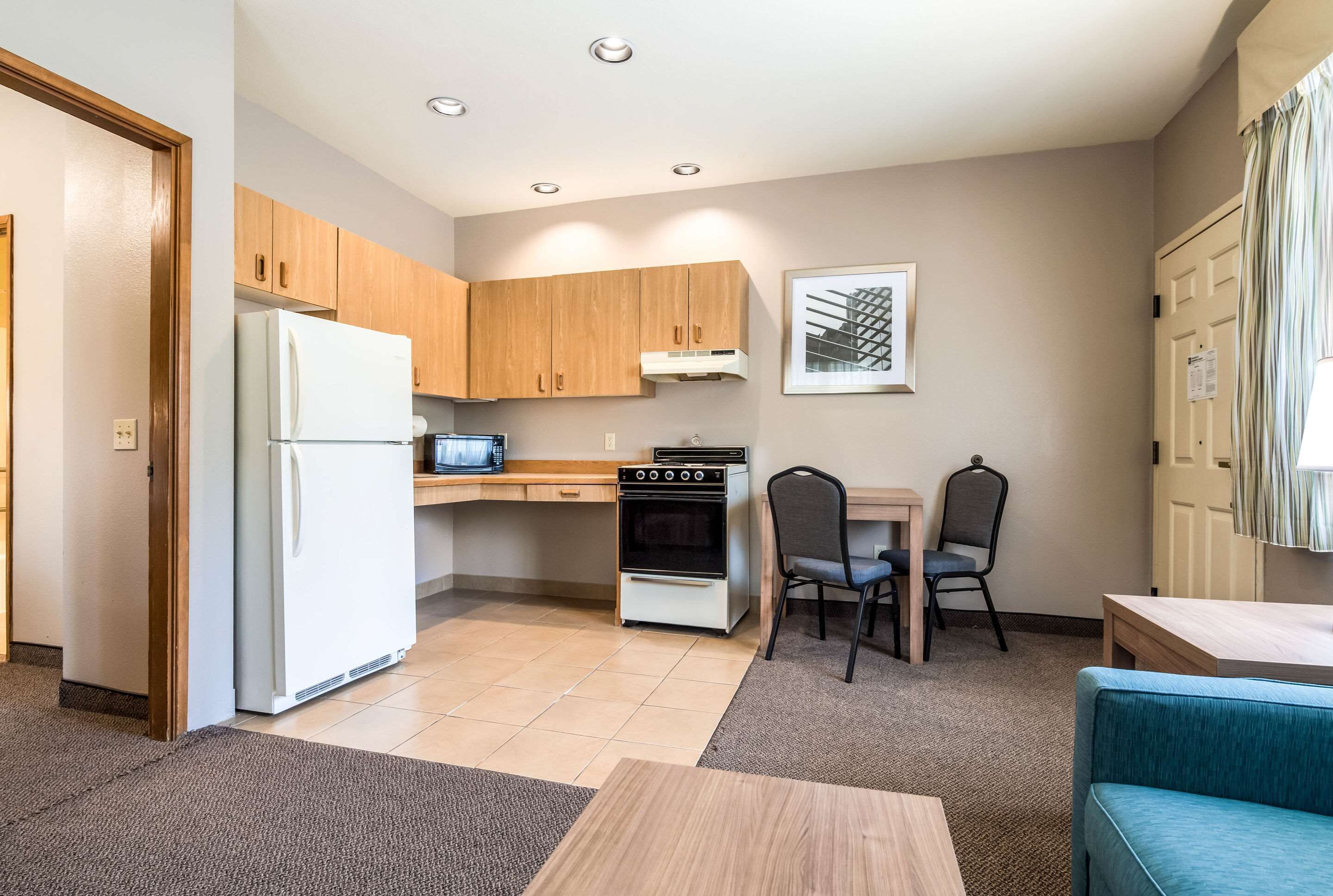 A compact kitchen with wooden cabinets, a white refrigerator, a microwave, and a stove. There is a dining area with a table and chairs, and a blue sofa.